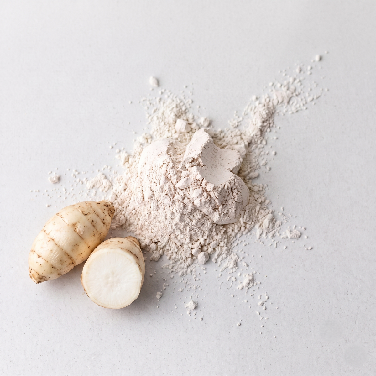 A pile of light beige powder with two raw arrow roots, one whole and one sliced open, arranged on a light gray background.