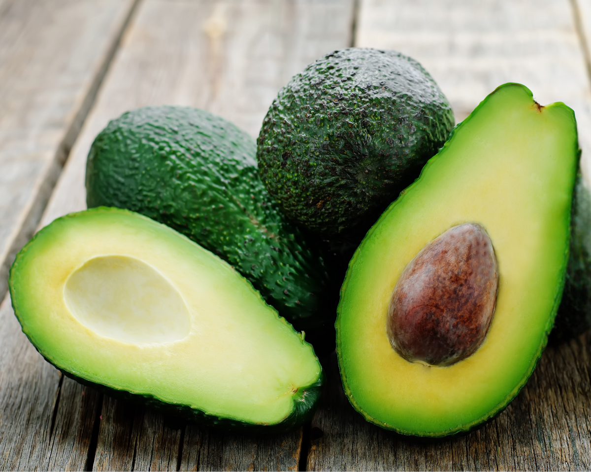 Avocados on a wooden surface with one cut in half.