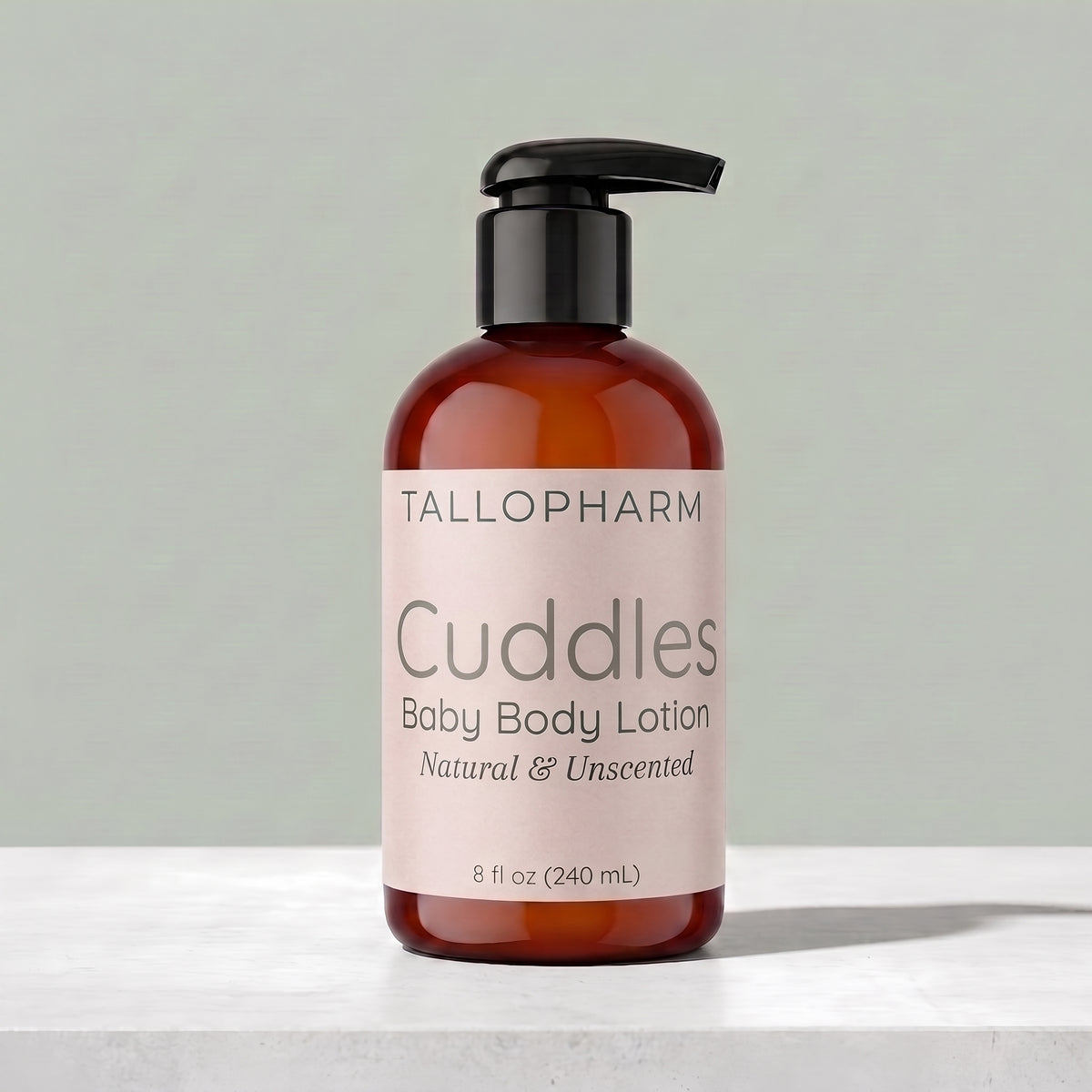 A bottle of Tallopharm Cuddles Baby Body Lotion with a black pump and a pale pink label, set on a light marble surface against a soft gray-green background.