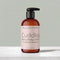 A bottle of Tallopharm Cuddles Baby Body Lotion with a black pump and a pale pink label, set on a light marble surface against a soft gray-green background.