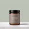 A jar of Tallopharm Wrap Body Butter on a light gray stone surface against a sage green background. The product is in an amber glass jar with a black lid and a muted taupe label.