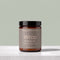 A jar of TALLOPHARM Wrap Body Butter in Mango & Bergamot scent, featuring an amber glass jar with a black lid and a muted taupe label, set on a light gray stone surface against a sage green background.