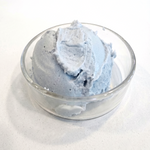 A scoop of light blue-gray whipped bergamot body butter in a small clear glass bowl, photographed on a plain light background.