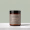 A jar of TALLOPHARM Wrap Body Butter on a light gray stone surface against a sage green background. The product is in an amber glass jar with a black lid and a taupe label.