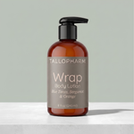 An 8 fl oz amber bottle of Tallopharm Wrap Body Lotion with a black pump dispenser and a taupe label, set on a light gray stone surface against a sage green background. Blue Tansy, Bergamot, Orange fragrance.