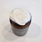 A jar of Tallopharm Wrap Lime Ginger & Sandalwood Body Butter, with a thick white cream piled on top, sits on a light, speckled countertop.