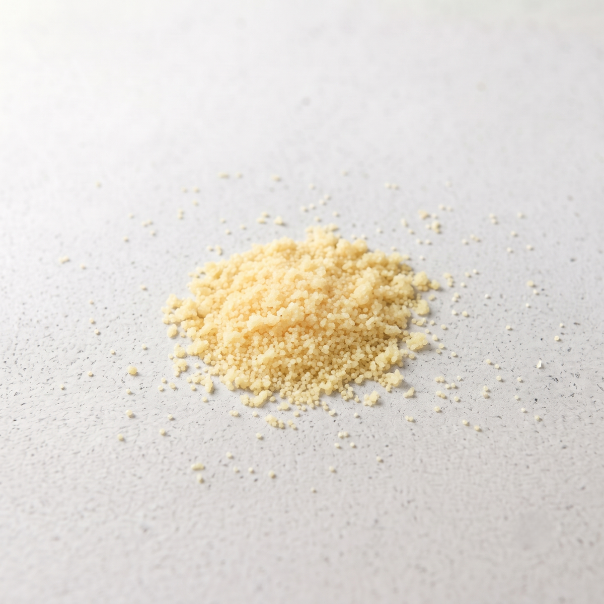 A small pile of fine pale candelilla scattered on a light gray textured surface.