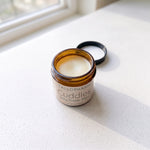 Daily Diaper Balm amber jar on light surface with lid off showing the balm.