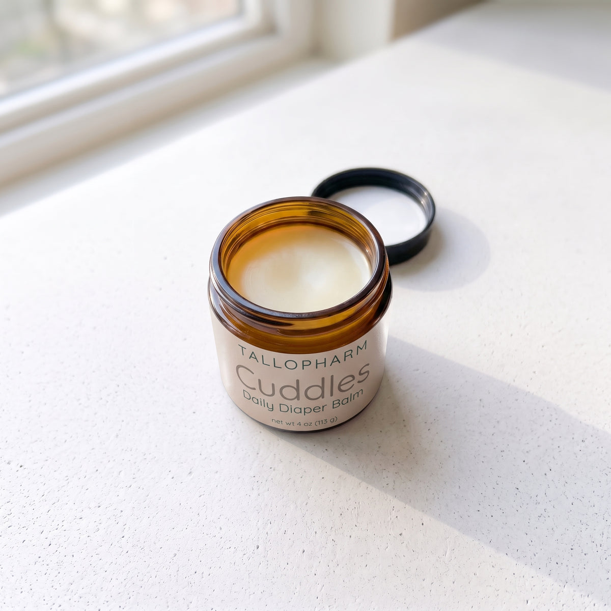 Daily Diaper Balm amber jar on light surface with lid off showing the balm.