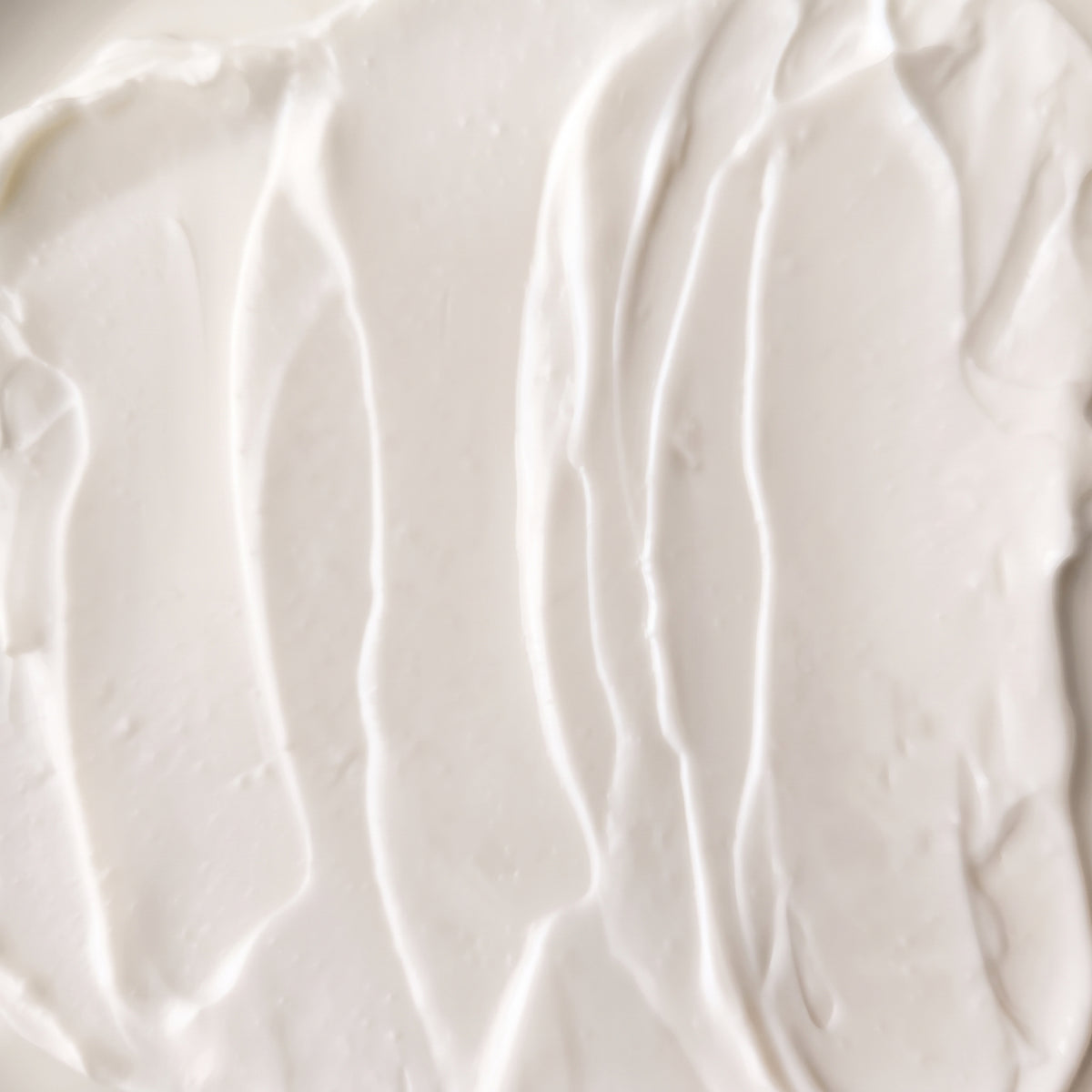 A close-up texture shot of a thick, creamy off-white cosmetic cream with soft vertical swirled lines.