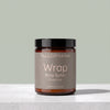A jar of Tallopharm Wrap Body Butter in Fresh Pear, featuring an amber glass jar, a black lid, and a taupe label, set on a light gray marble surface against a sage green background.