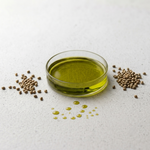 Glass bowl of green oil with hemp seed on a light background