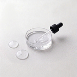 Glass dropper with black cap over a small glass container of clear Hyaluronic Acid on a light gray background