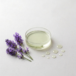 Clear glass container with light golden oil, lavender flowers, and small round oil drops on a light gray background