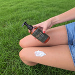 A person sitting on green grass holds a bottle of Fend Body Lotion. A dollop of white lotion is smeared on their thigh.