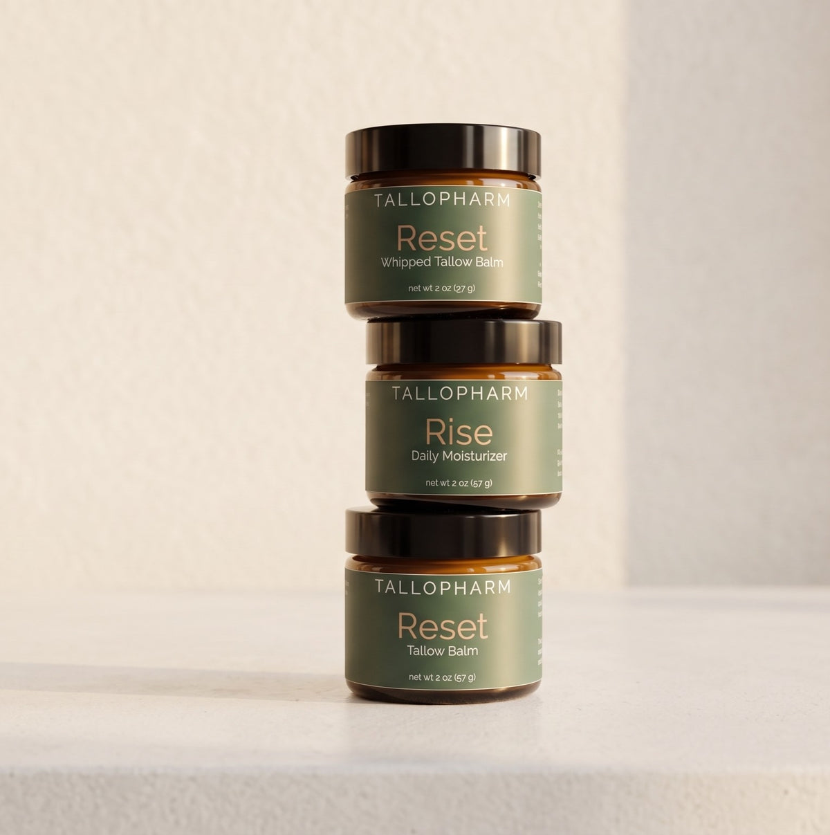 Three amber glass jars of TALLOPHARM products stacked vertically on a light beige surface against a textured beige wall. The top jar is Reset Whipped Tallow Balm, the middle is Rise Daily Moisturizer, and the bottom is Reset Tallow Balm.