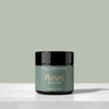A jar of Tallopharm Reset Tallow Balm sits on a light concrete surface against a muted sage green background. The jar has a black lid and a sage green label with gold and white text.