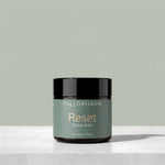 A jar of Tallopharm Reset Tallow Balm sits on a light concrete surface against a muted sage green background. The jar has a black lid and a sage green label with gold and white text.