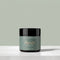 A jar of Tallopharm Reset Tallow Balm sits on a light concrete surface against a muted sage green background. The jar has a black lid and a sage green label with gold and white text.