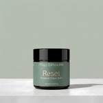 A jar of Tallopharm Reset Whipped Tallow Balm sits on a white concrete surface against a sage green background.