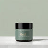 A jar of Tallopharm Rest Overnight Moisturizer with a sage green label and black lid, sitting on a white concrete surface against a sage green background.