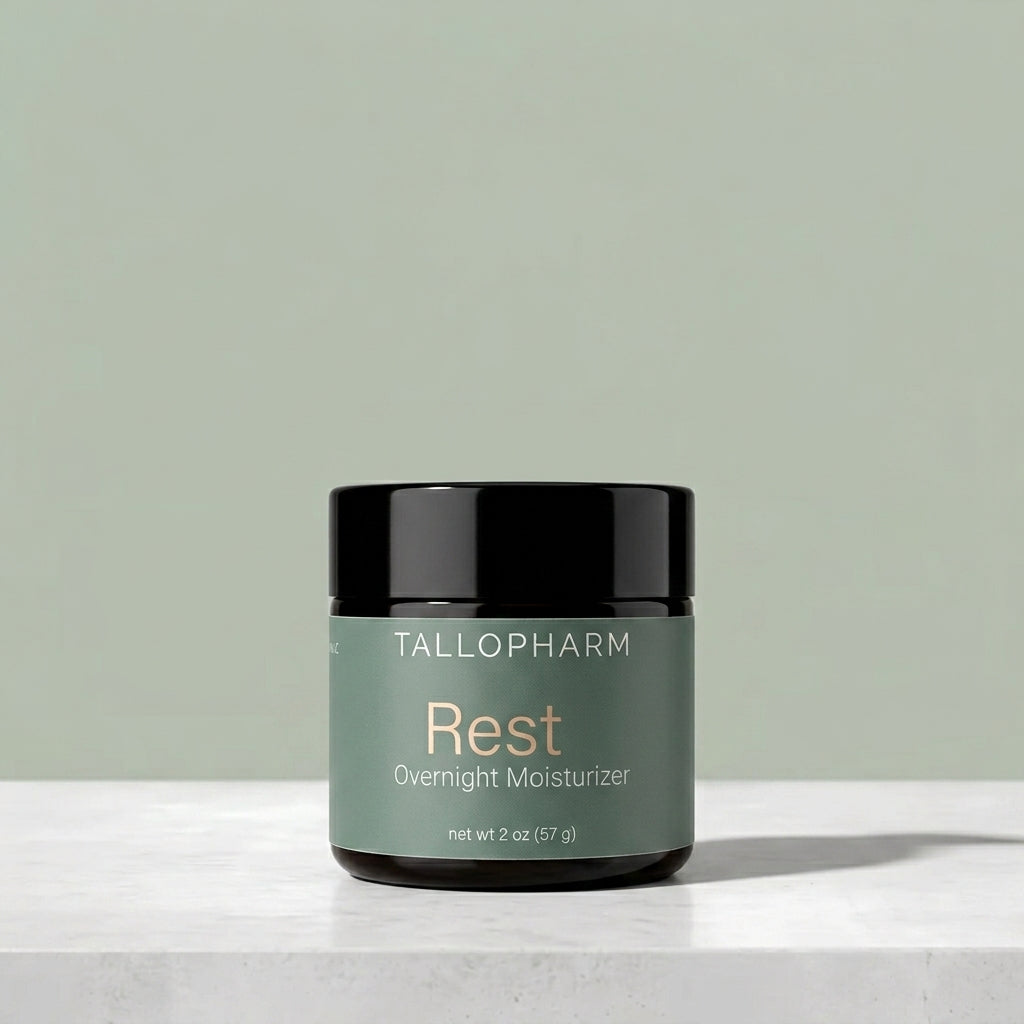 A jar of Tallopharm Rest Overnight Moisturizer with a sage green label and black lid, sitting on a white concrete surface against a sage green background.