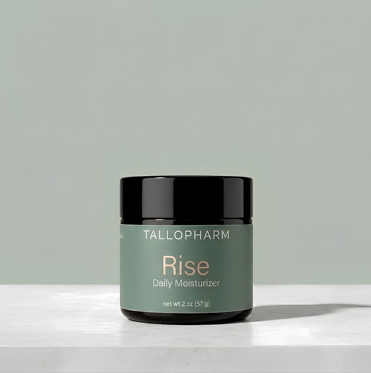 A jar of TALLOPHARM Rise Daily Moisturizer with a sage green label and black lid, sitting on a white concrete surface against a matching sage green background.