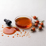 Glass bowl with amber rosehip oil, dropper, and rosehips on a light background
