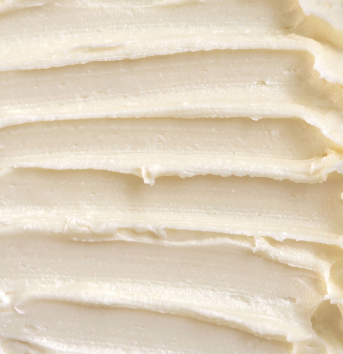 A close-up texture shot of thick, creamy off-white rich cream with horizontal ridges.