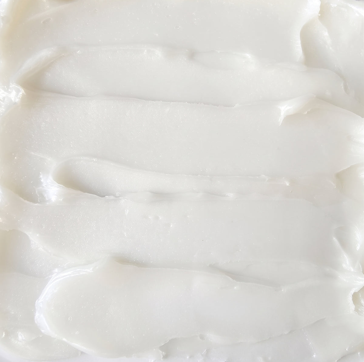 A close-up texture shot of a thick, creamy off-white cream, showing smooth horizontal swaths and a glossy, slightly translucent surface.