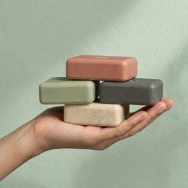 Hand holding four stacked soap bars against a plain background