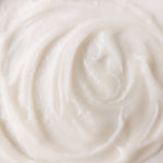 A close-up texture shot of a thick, creamy off-white cosmetic cream with a swirled pattern.