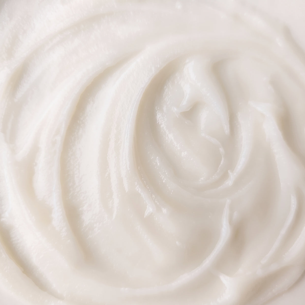 A close-up texture shot of a thick, creamy off-white cosmetic cream with a swirled pattern.