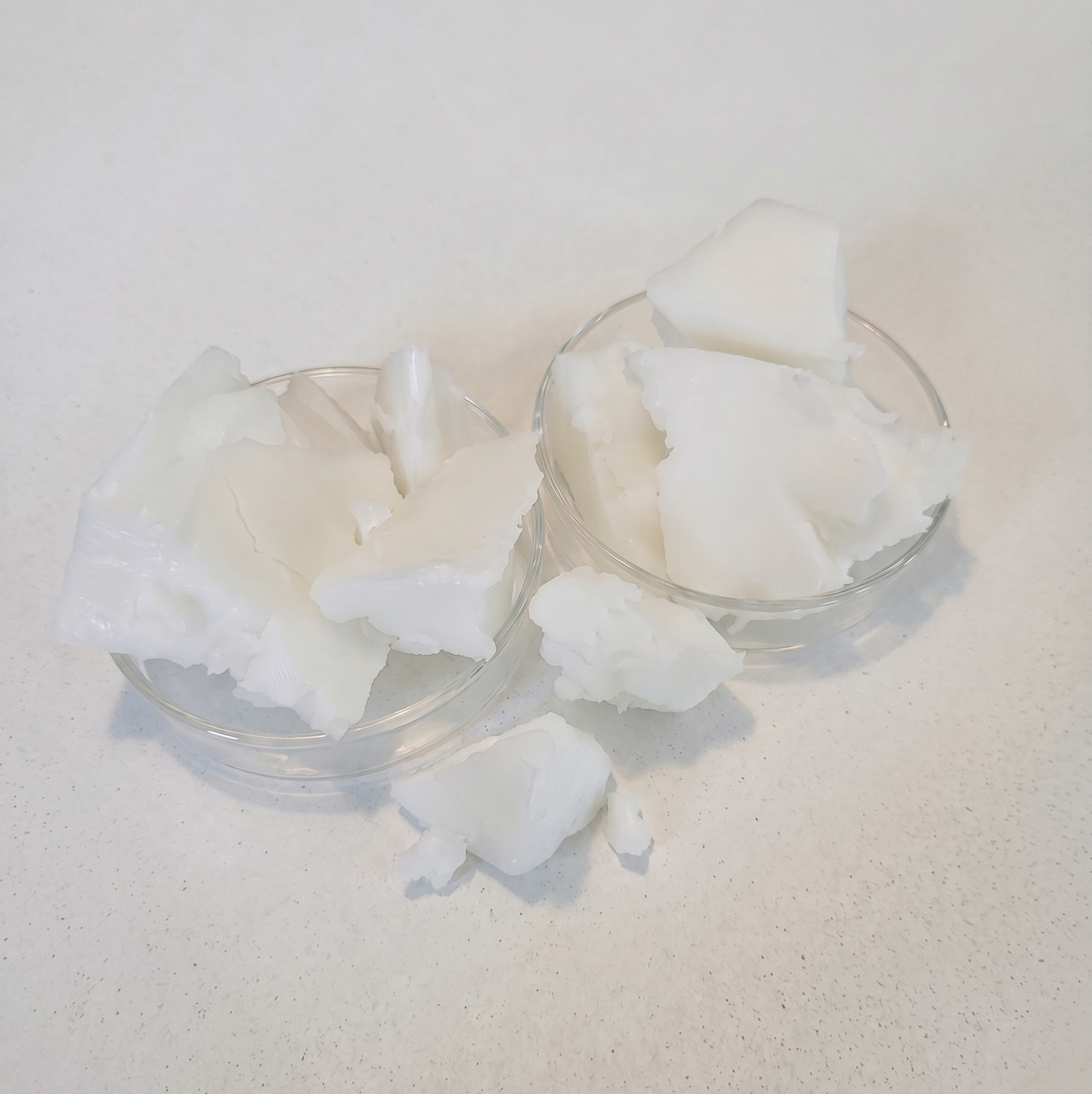 White solid beef tallow chunks displayed in two small clear glass bowls on a light beige textured surface.