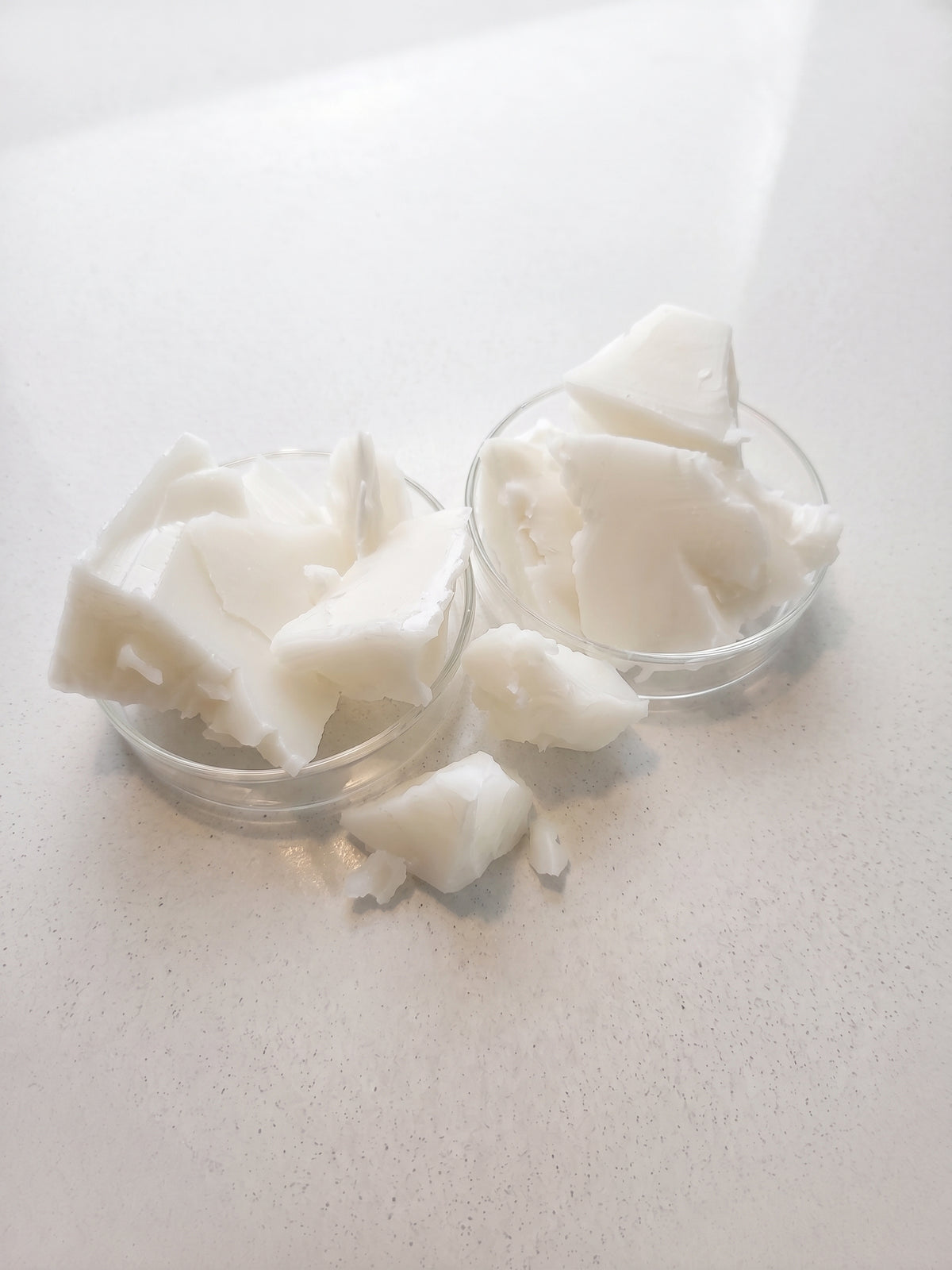 White solid beef tallow chunks displayed in two small clear glass bowls on a light beige surface.